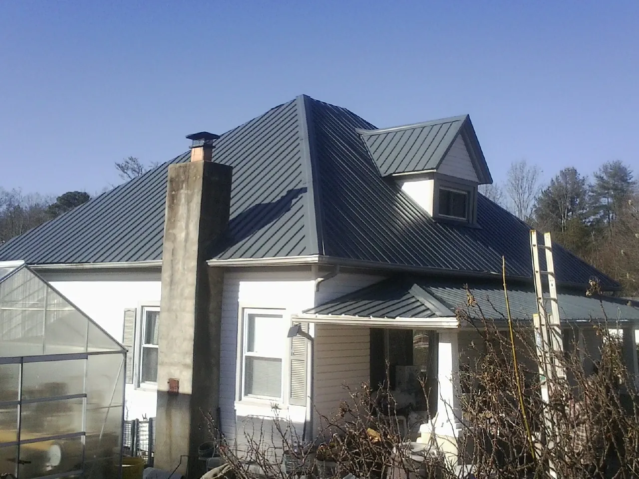 Dark blue standing seam metal roof on a white farmhouse with dormer — Slate & Tile Roof Repair by Roofing Brothers in Wiggins