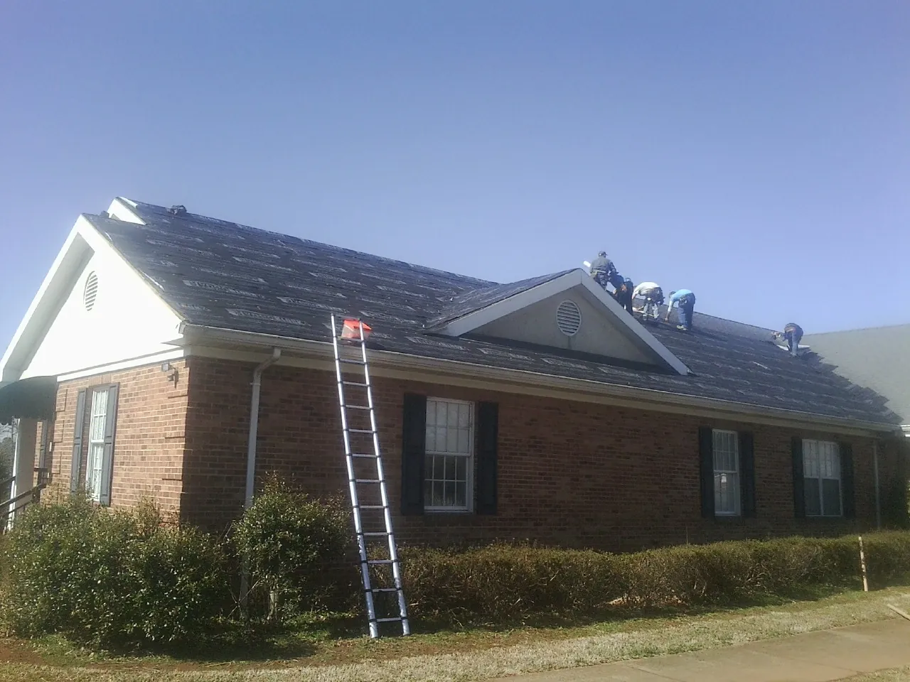 Crew tearing shingles off a brick ranch roof with a ladder set — Emergency Roof Repair work by our crew in Wiggins