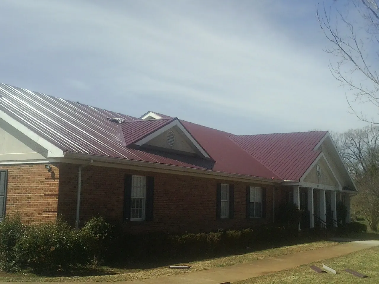 Red metal roof with gabled entries on a long brick building, from a Hail Damage Roof Repair job in Wiggins